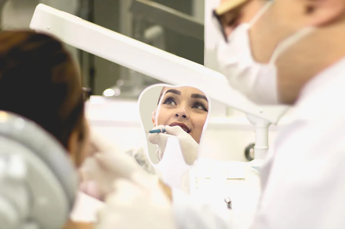 Dentista na clínica odontológica Acessa Odontologia, o Dr Rafael atende uma cliente que segura um espelho em forma de dente e seu rosto aparece no reflexo.